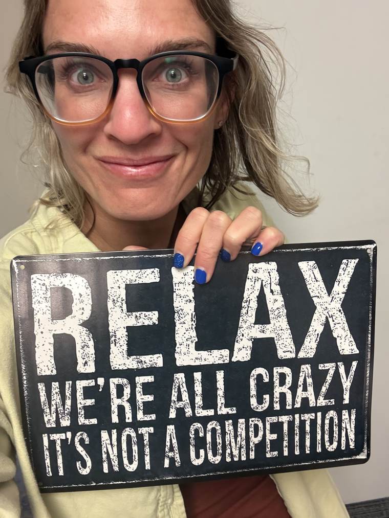 Mandi Kane smiling and holding a sign that reads: Relax, we're all crazy, it's not a competition